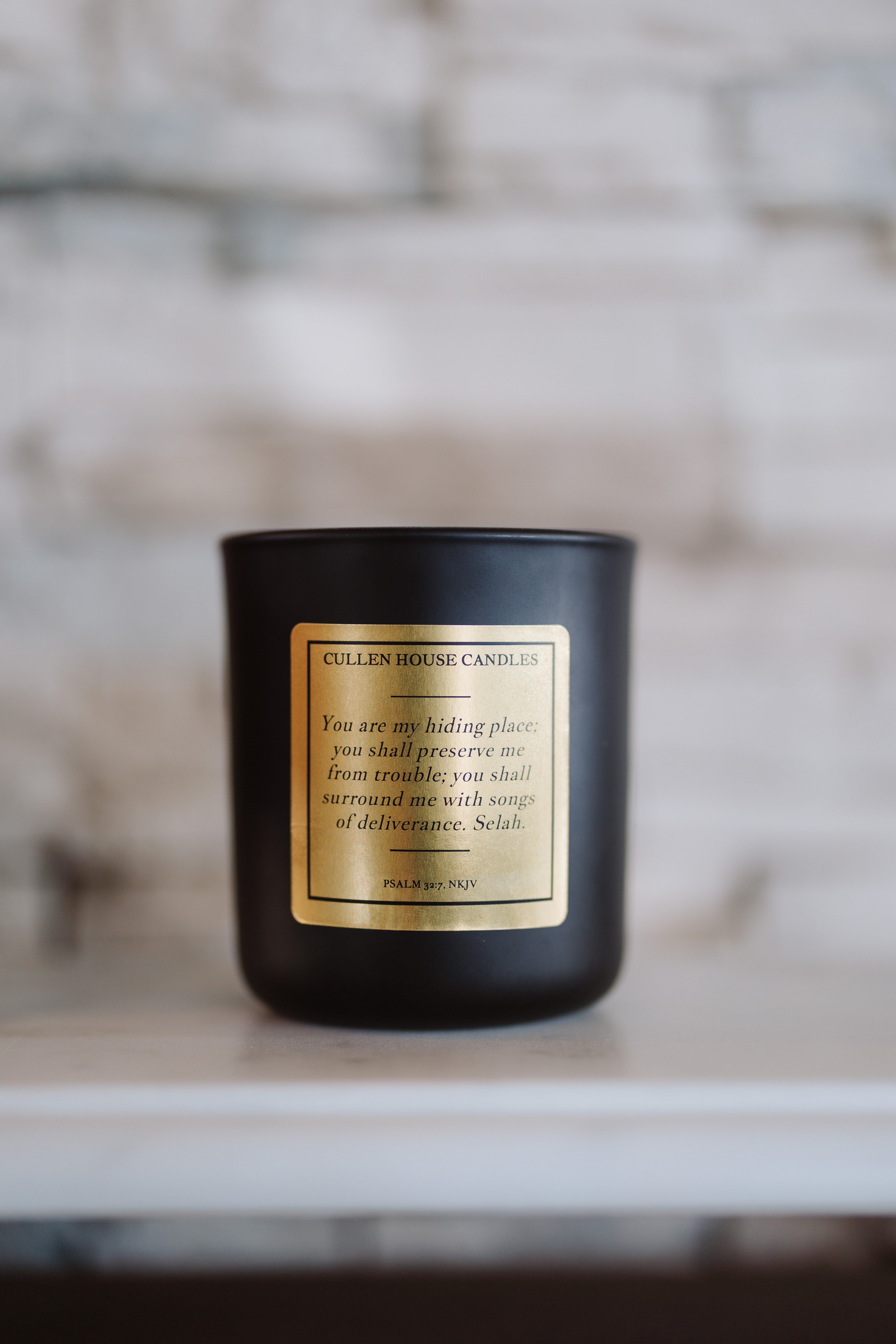 Black candle with a gold label on a neutral background