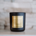 Black candle with a gold label on a wooden surface with a blurred background