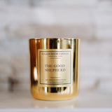 Gold candle jar labeled 'The Good Shepherd' by Cullen House Candles on a marble surface.
