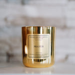 Gold candle with 'Prayer' label on a marble surface