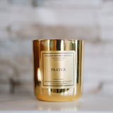 Gold candle with 'Prayer' label on a marble surface