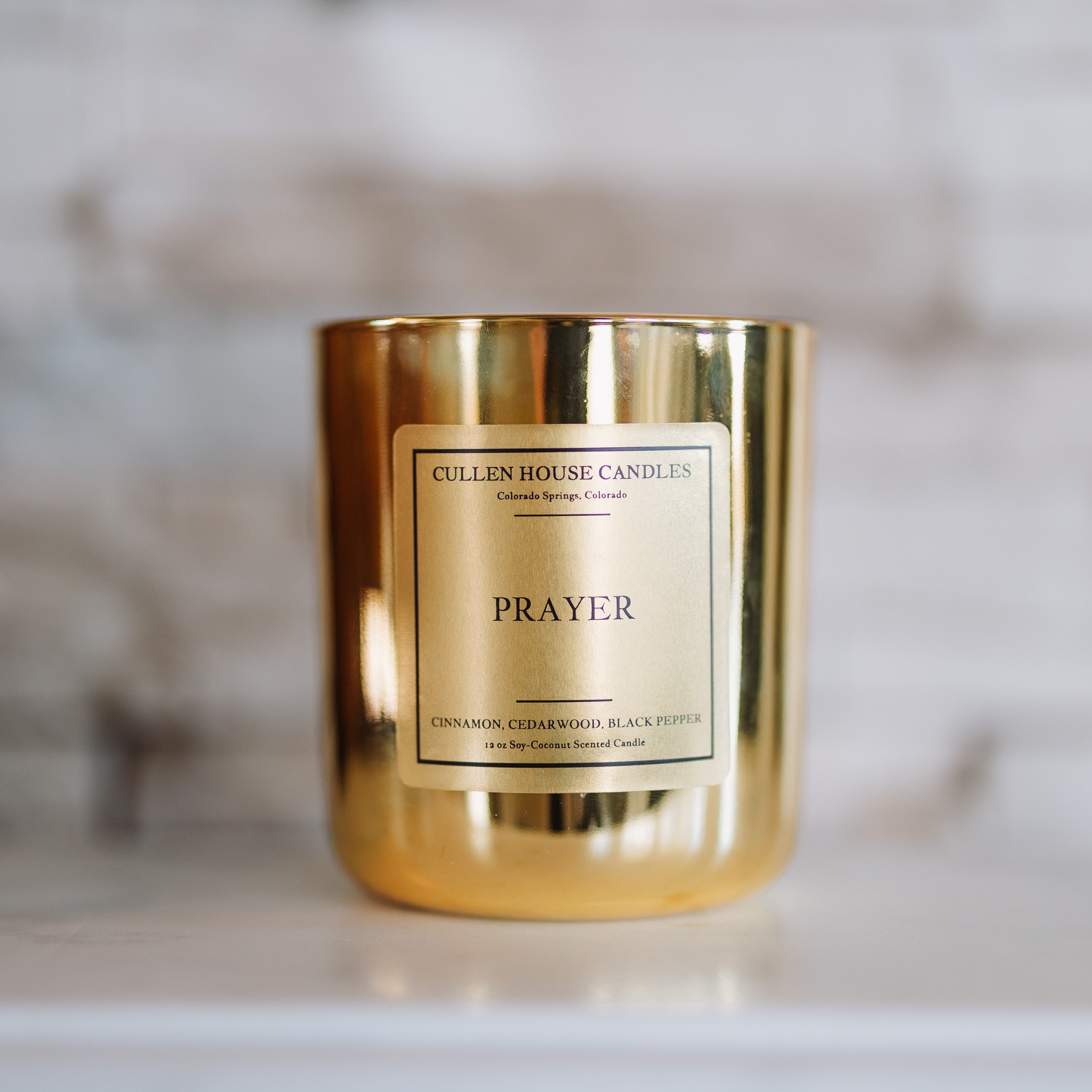 Gold candle with 'Prayer' label on a marble surface