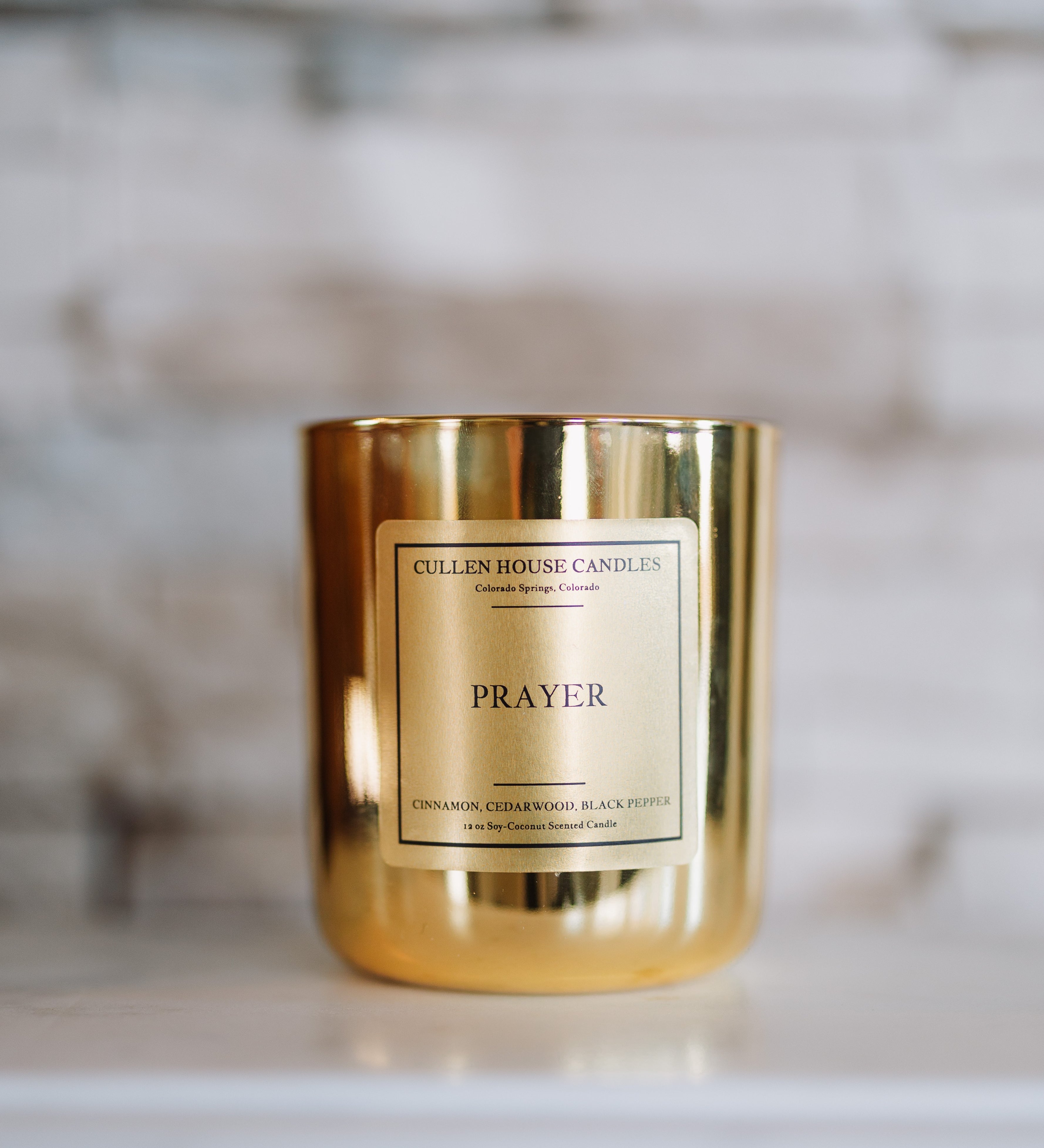 Gold candle with 'Prayer' label on a marble surface