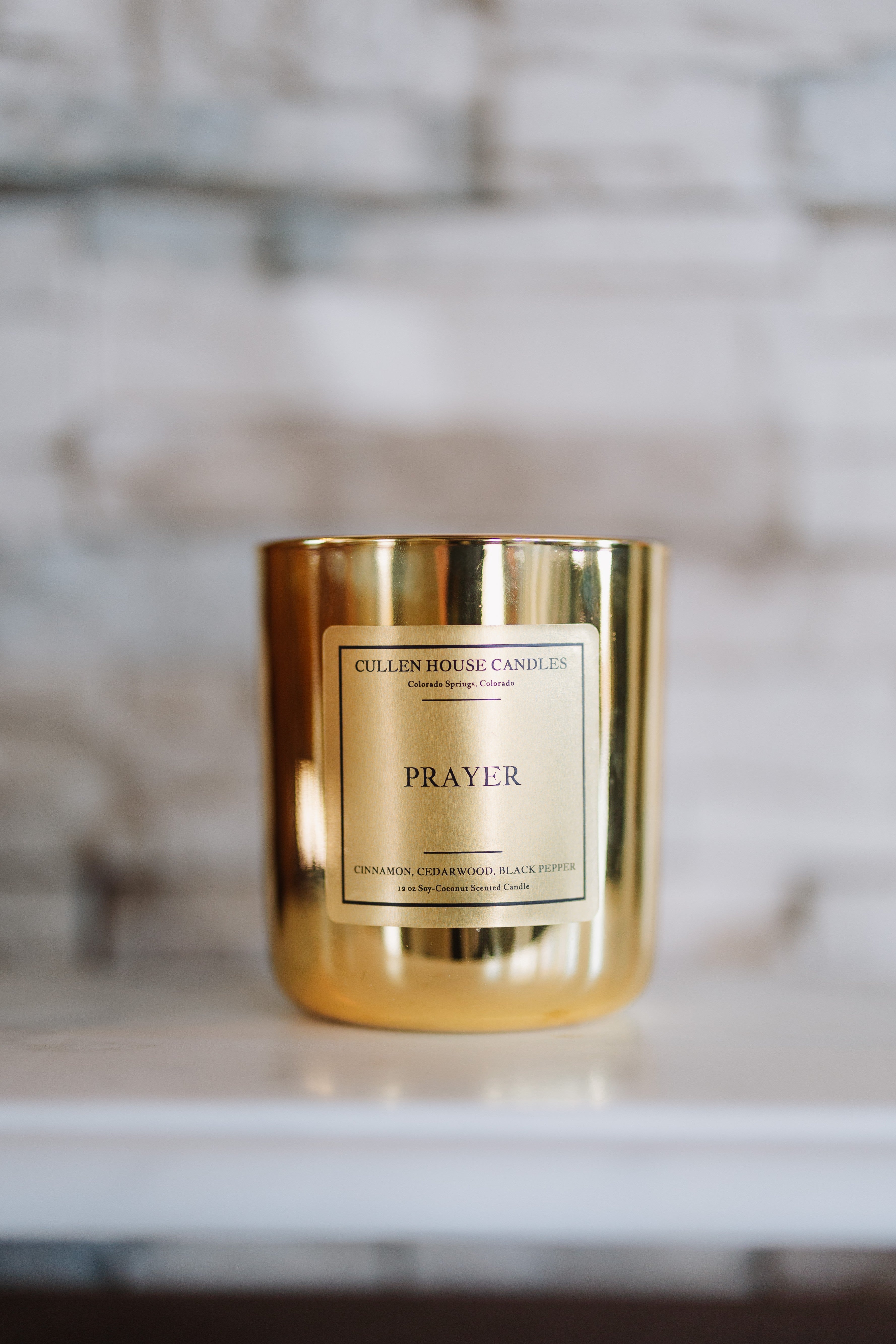 Gold candle with 'Prayer' label on a marble surface