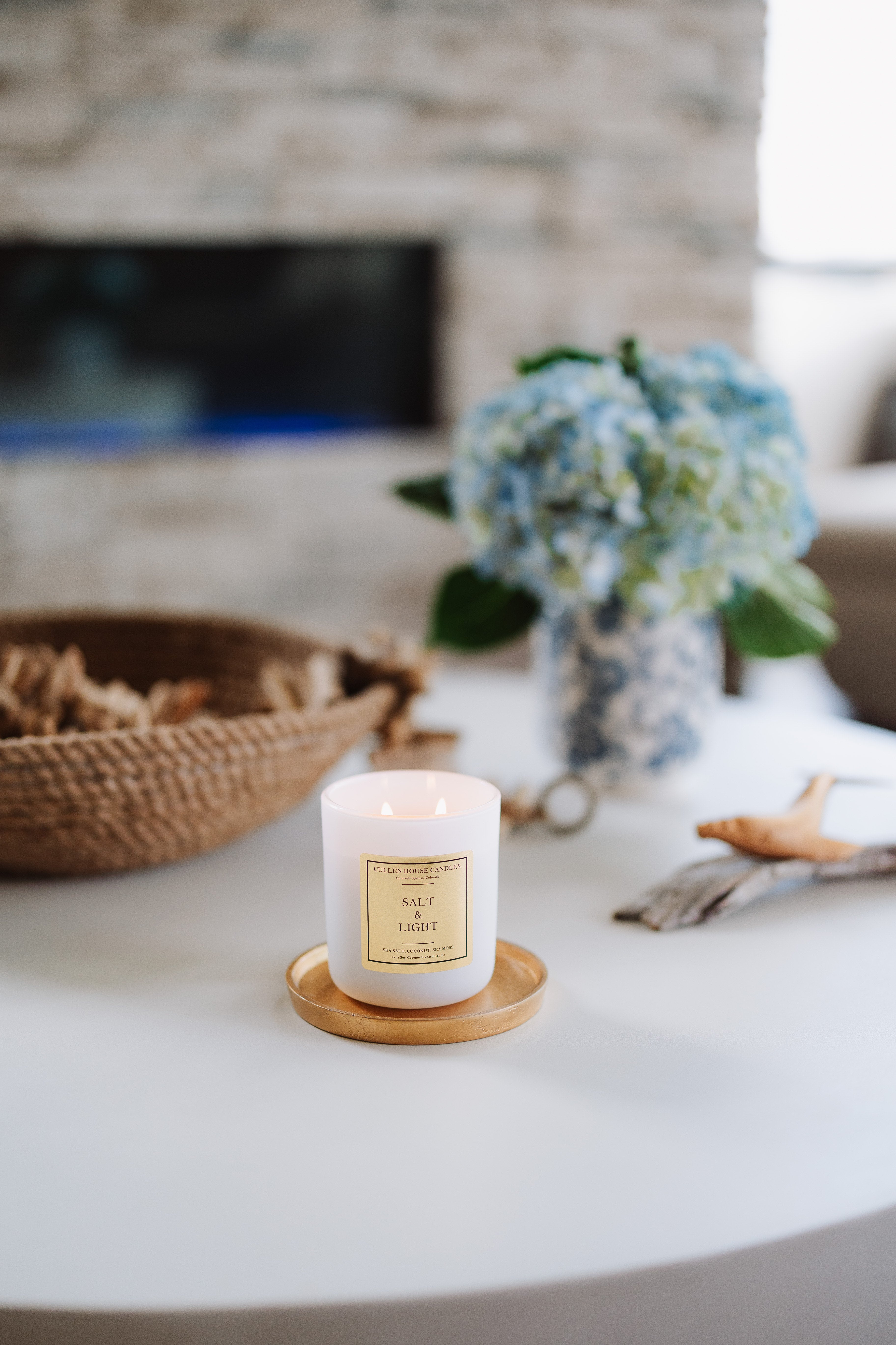 Candle on a wooden coaster with a fireplace and decorative items in the background