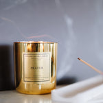 Gold candle labeled 'Prayer' on a marble surface with a blurred background
