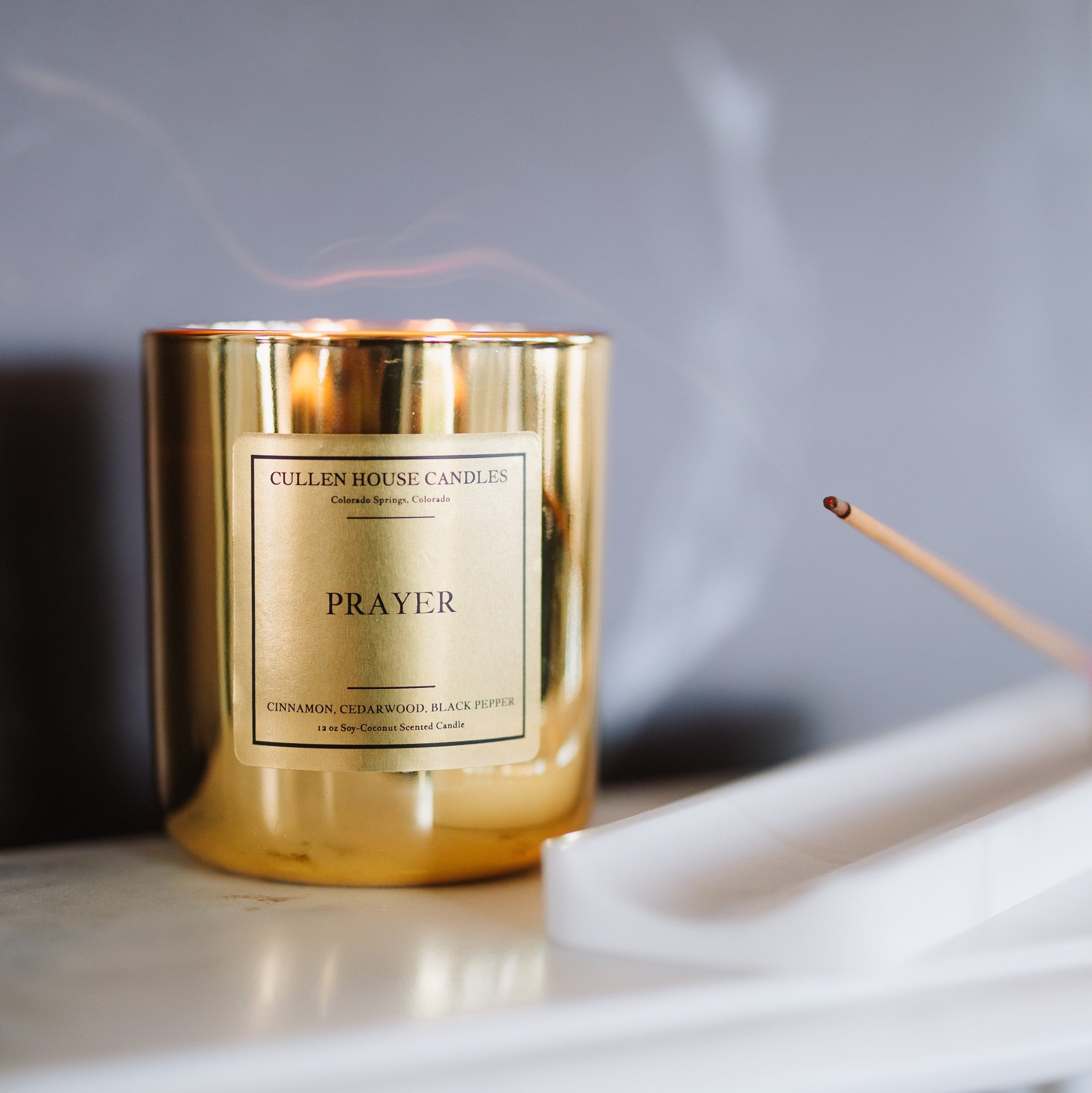 Gold candle labeled 'Prayer' on a marble surface with a blurred background