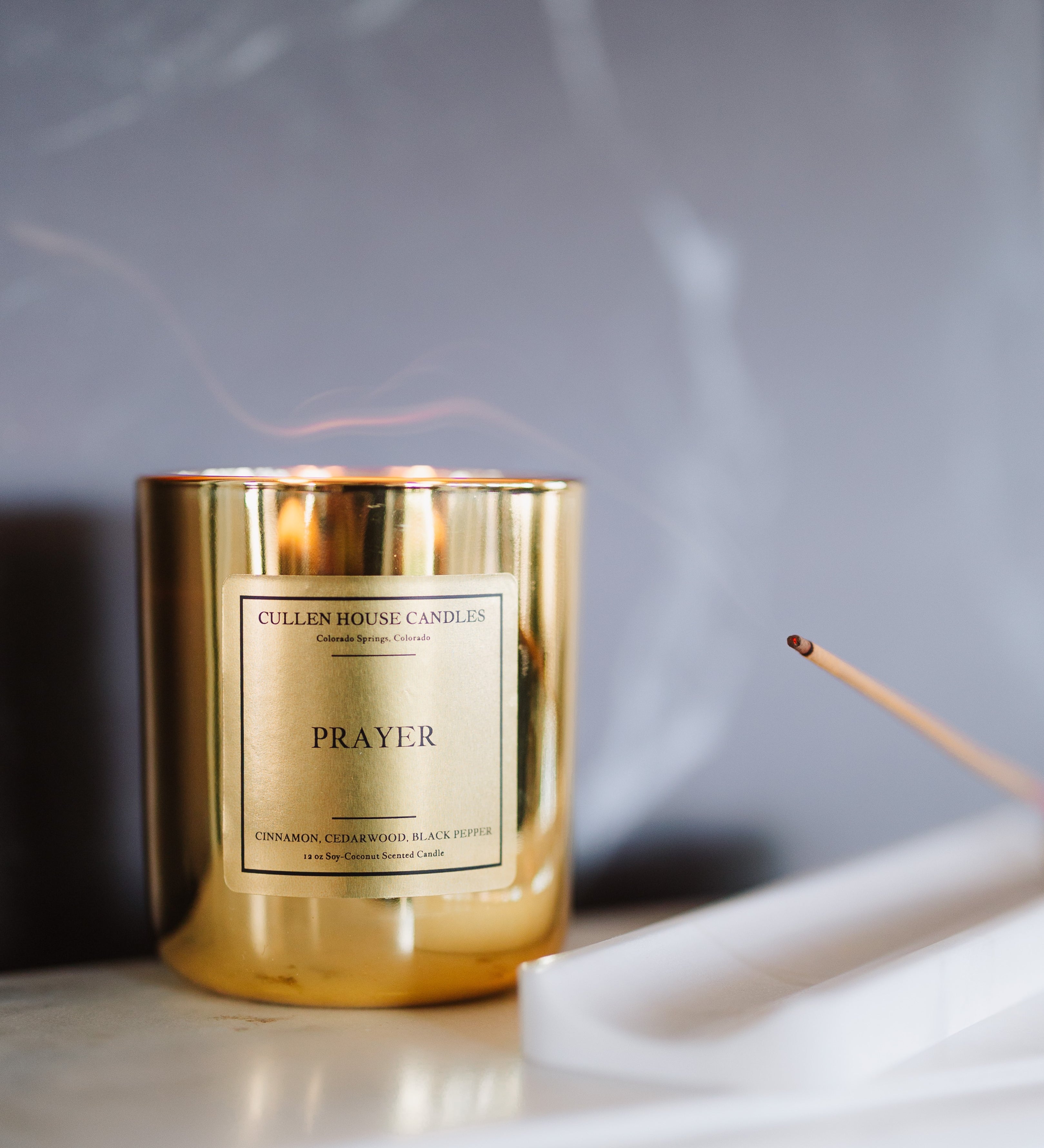 Gold candle labeled 'Prayer' on a marble surface with a blurred background
