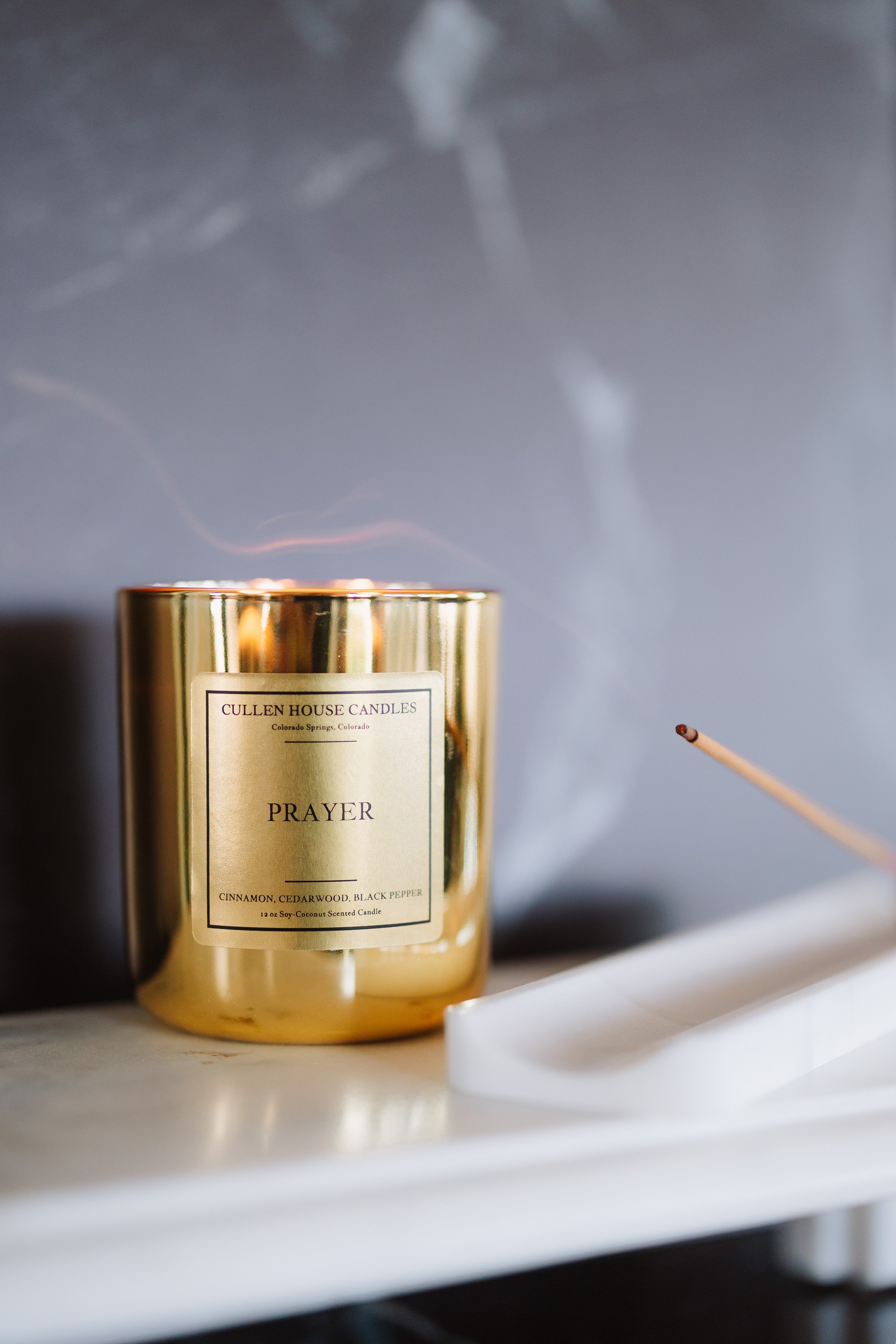 Gold candle labeled 'Prayer' on a marble surface with a blurred background