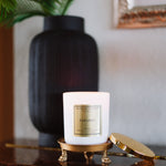 Candle labeled 'Paradise' on a decorative stand with a vase and plant in the background.