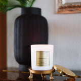 Candle labeled 'Paradise' on a decorative stand with a vase and plant in the background.