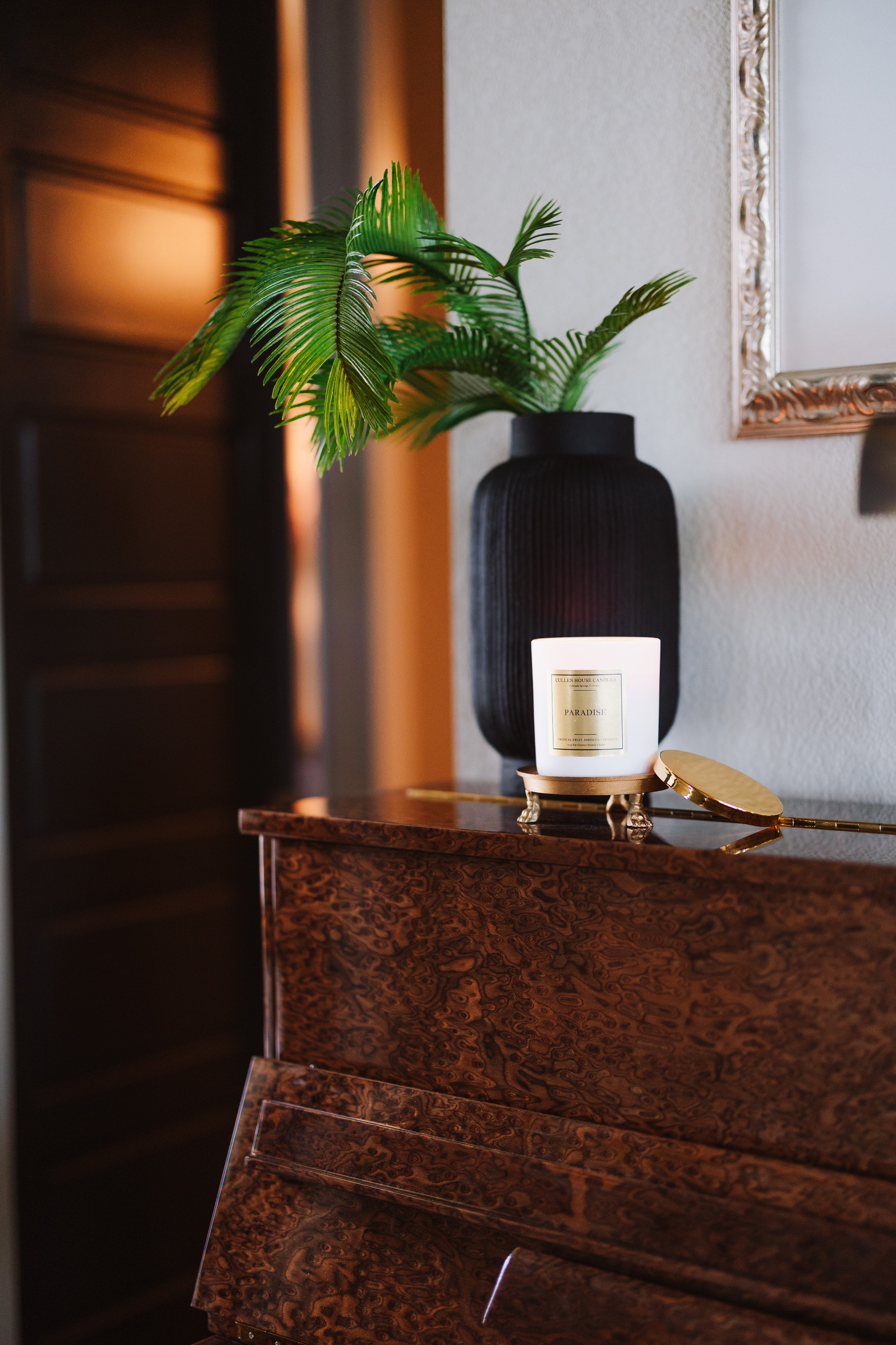 Decorative setting with a plant, vase, and candle on a wooden surface.