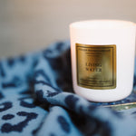White candle with a gold label on a blue patterned surface