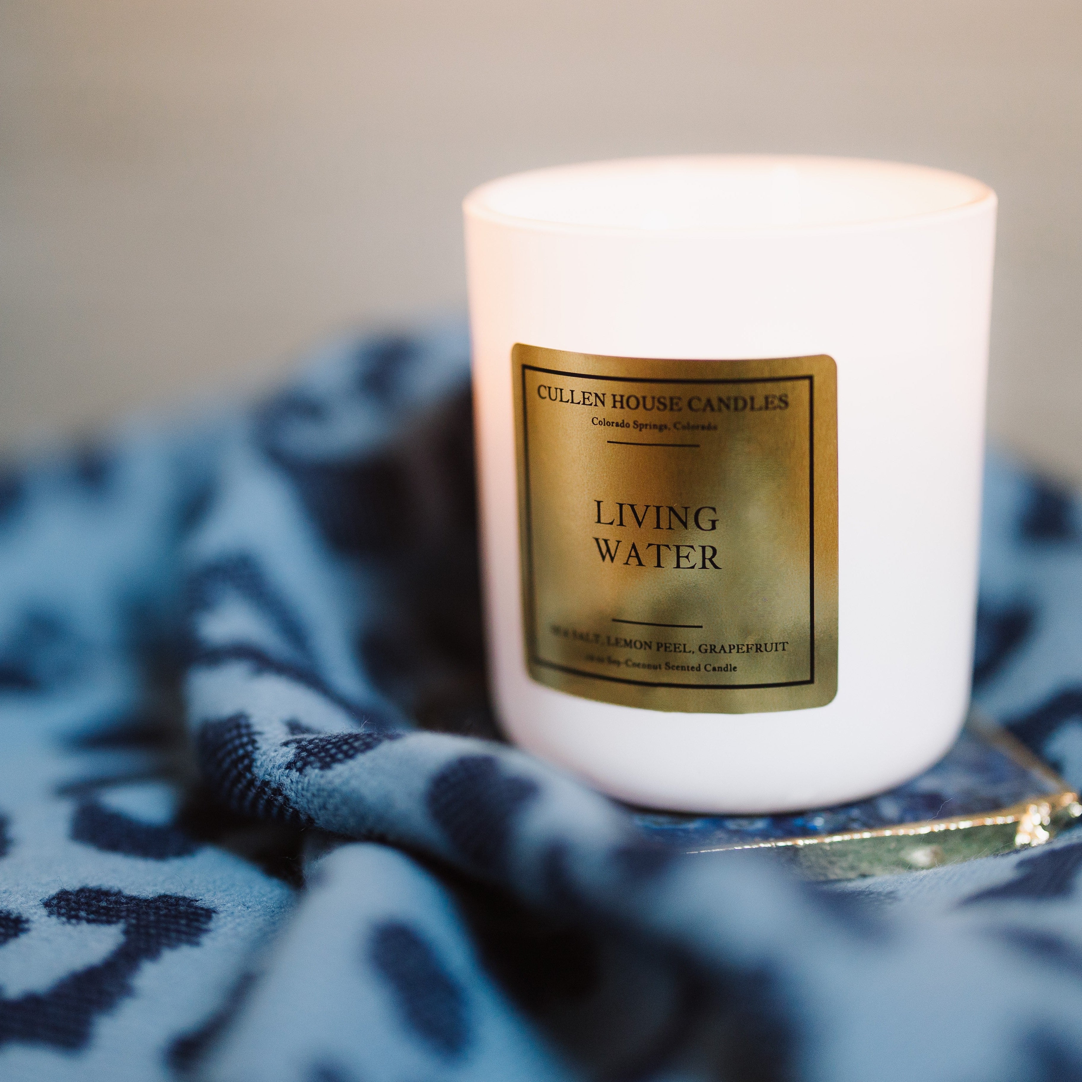 White candle with a gold label on a blue patterned surface