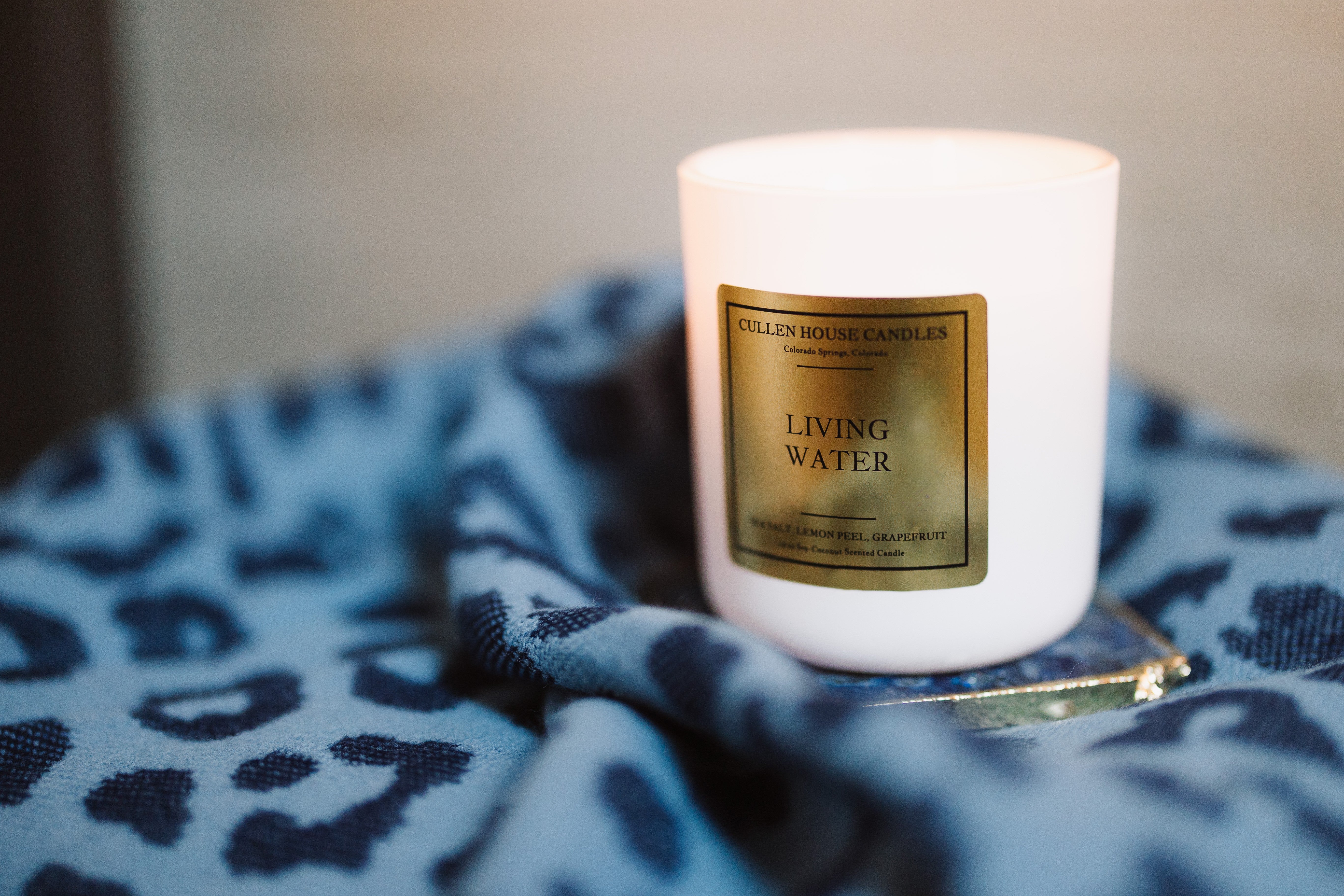 White candle with a gold label on a blue patterned surface