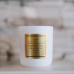 White candle with a gold label on a neutral background