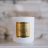 White candle with a gold label on a neutral background