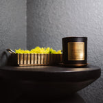 Candle with a decorative box on a dark surface against a gray wall