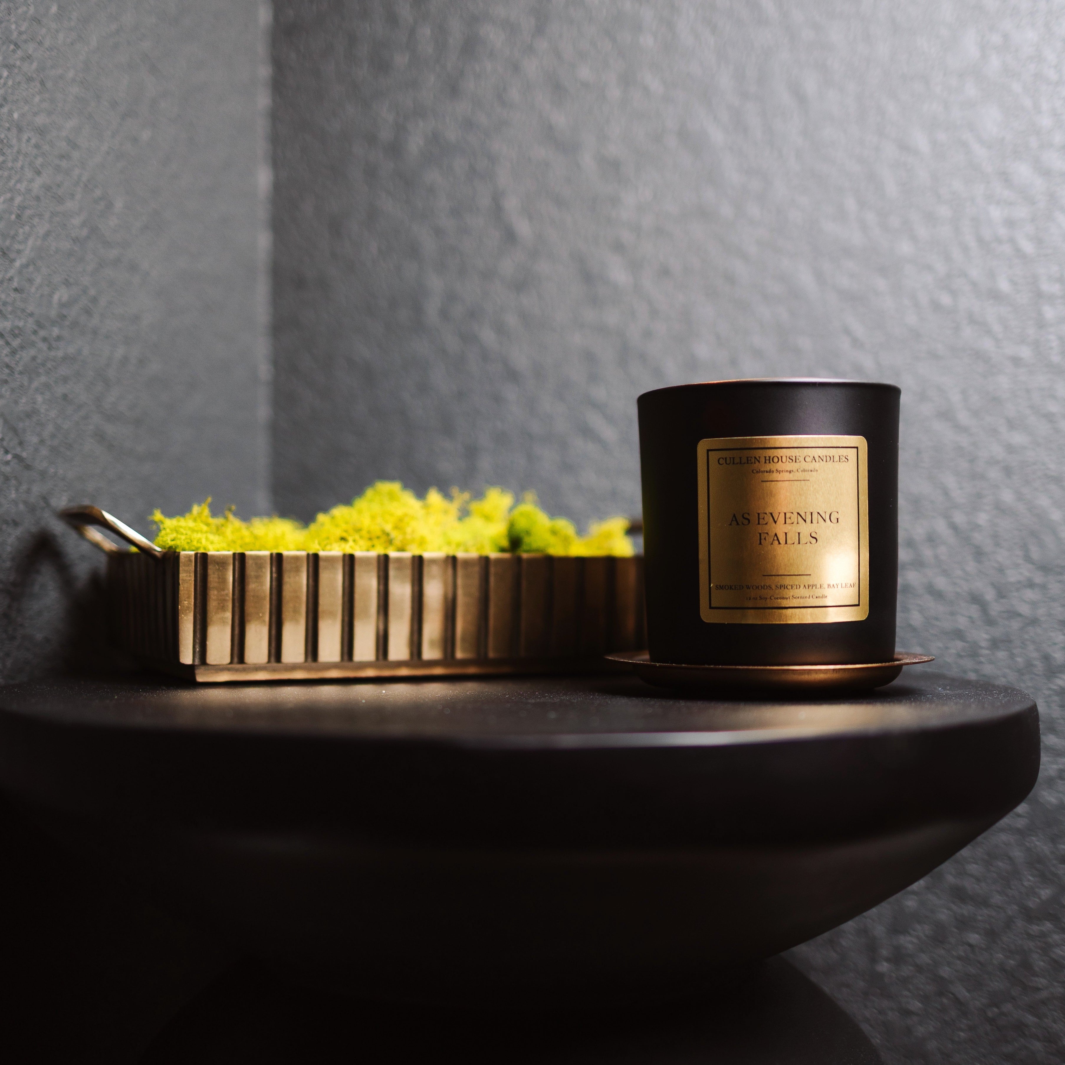 Candle with a decorative box on a dark surface against a gray wall
