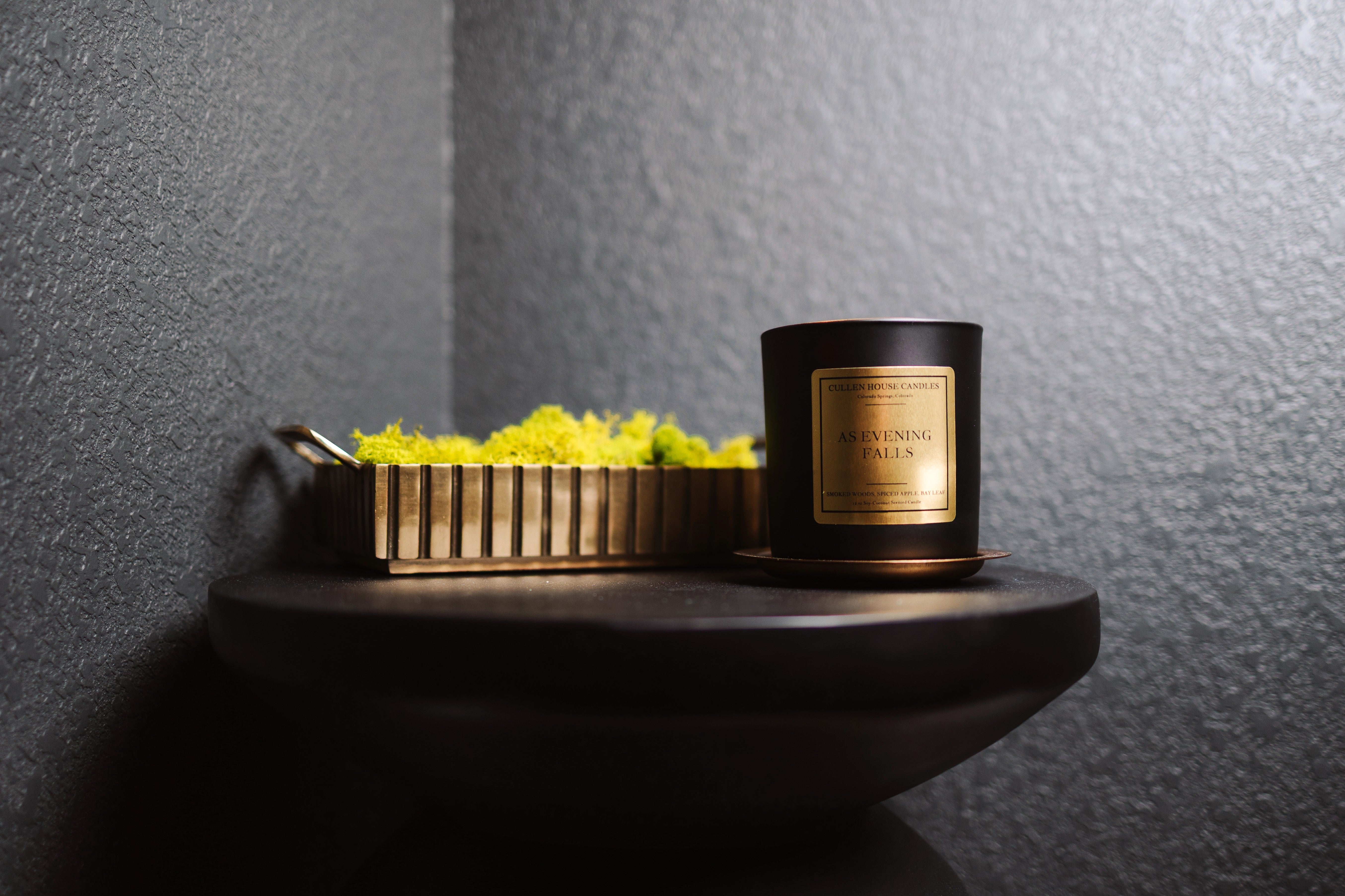 Candle with a decorative box on a dark surface against a gray wall
