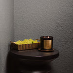 Black candle with gold label on a dark surface against a gray wall