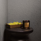 Black candle with gold label on a dark surface against a gray wall