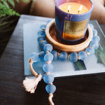 Candle in a decorative holder on a book with a blue beaded bracelet nearby