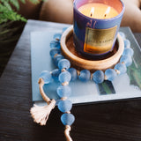 Candle in a decorative holder on a book with a blue beaded bracelet nearby