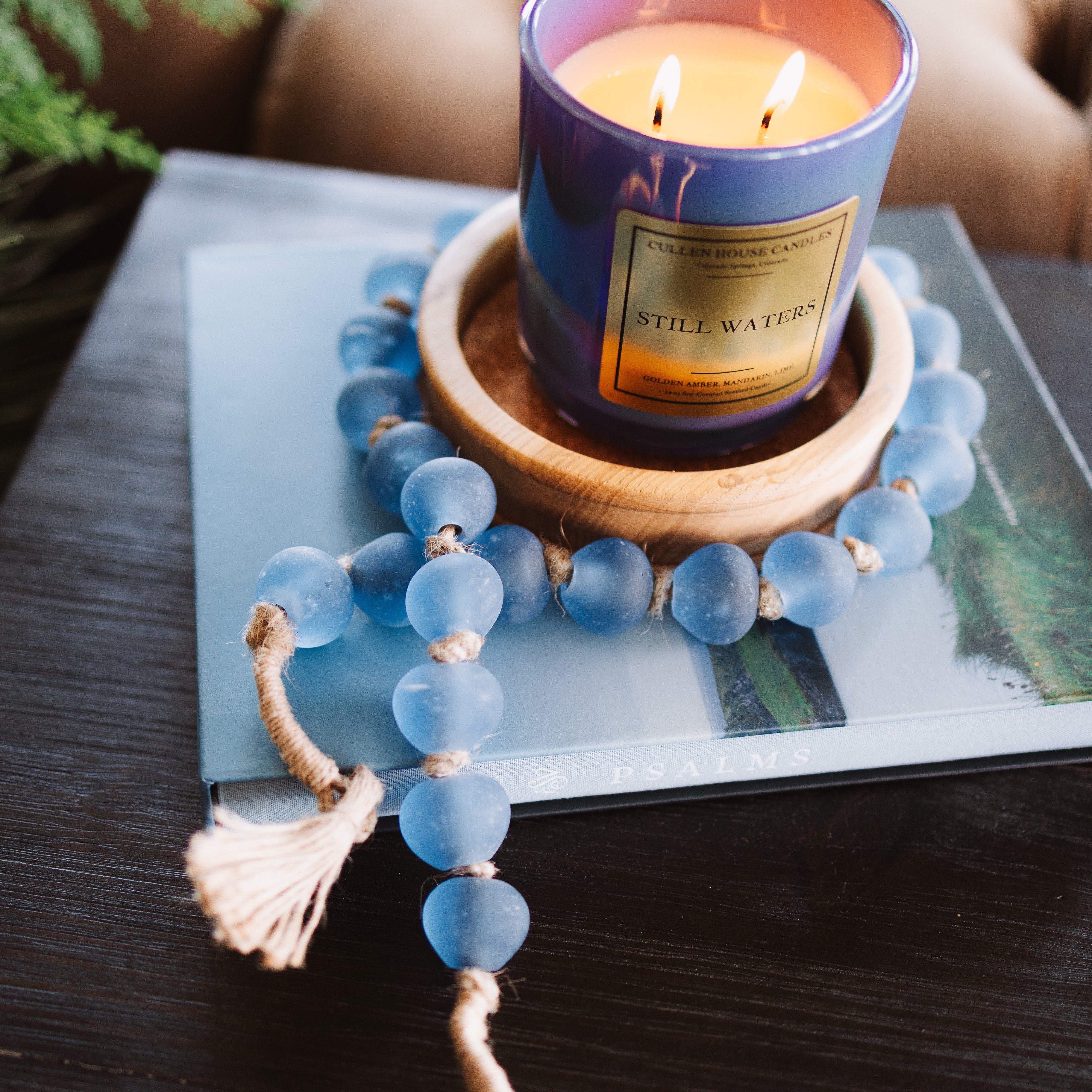 Candle in a decorative holder on a book with a blue beaded bracelet nearby