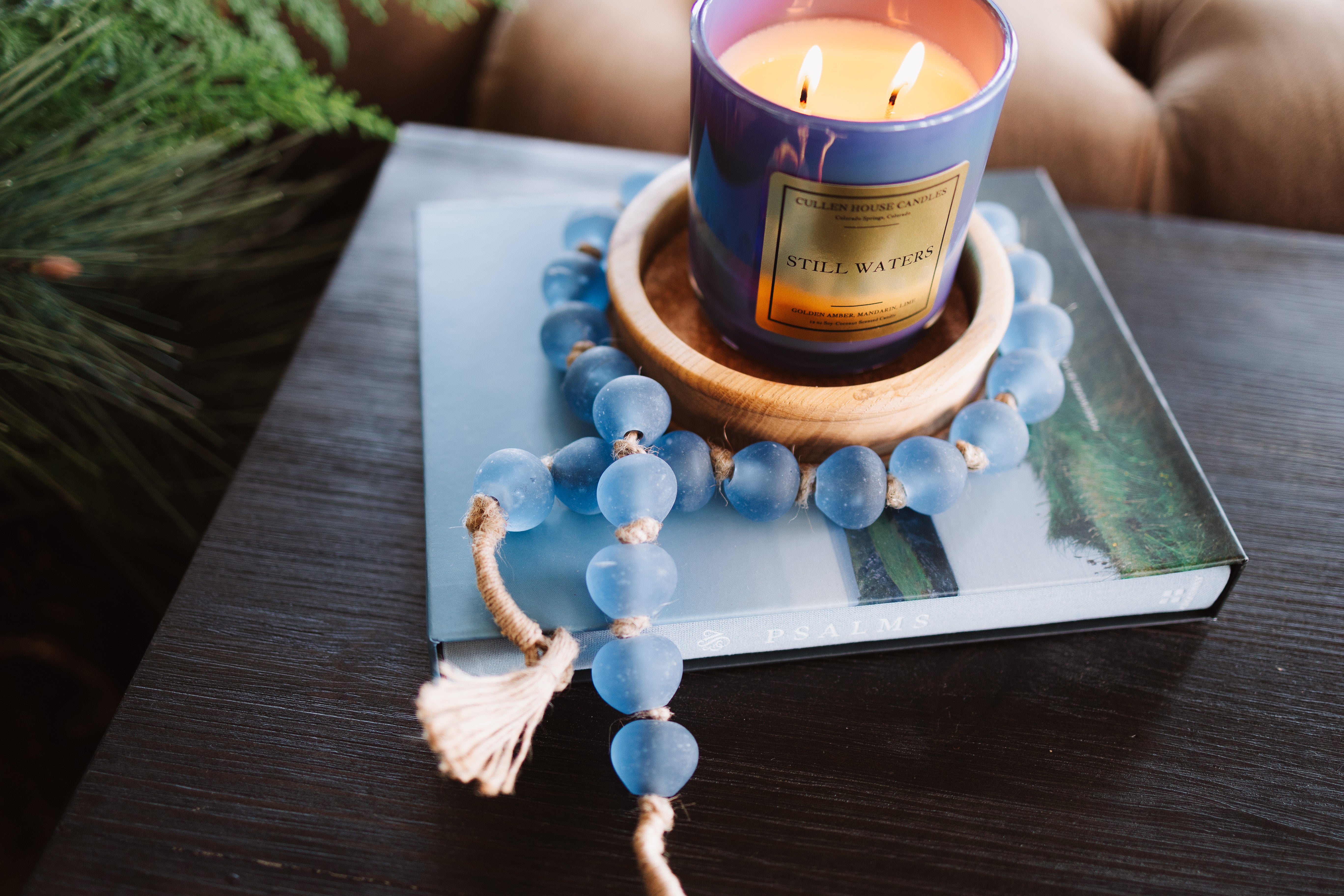 Candle in a decorative holder on a book with a blue beaded bracelet nearby