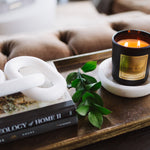 Candle on a coaster with books and a plant on a tray, against a couch background