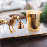 Gold candle holder with a horse design on a marble tray, featuring a lit candle.