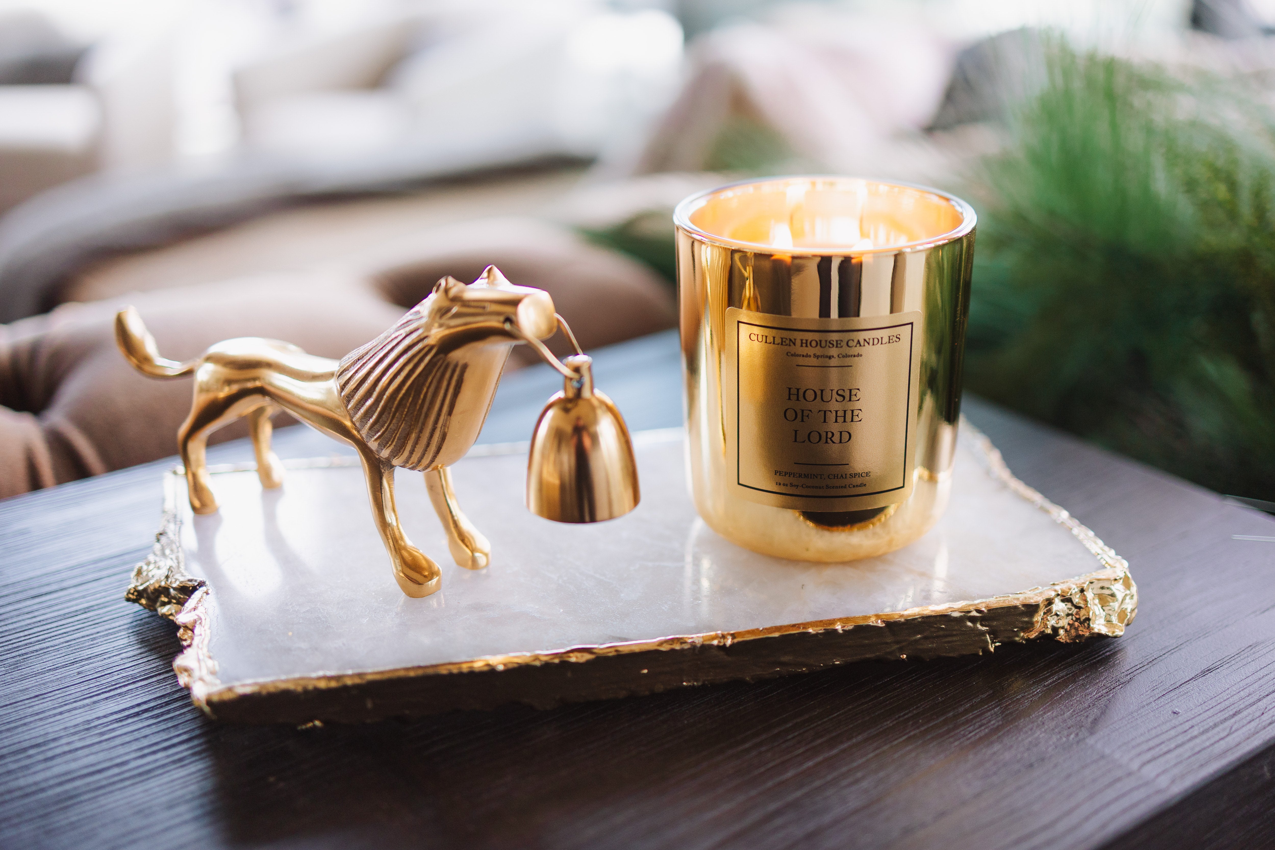 Gold candle holder with a horse design on a marble tray, featuring a lit candle.