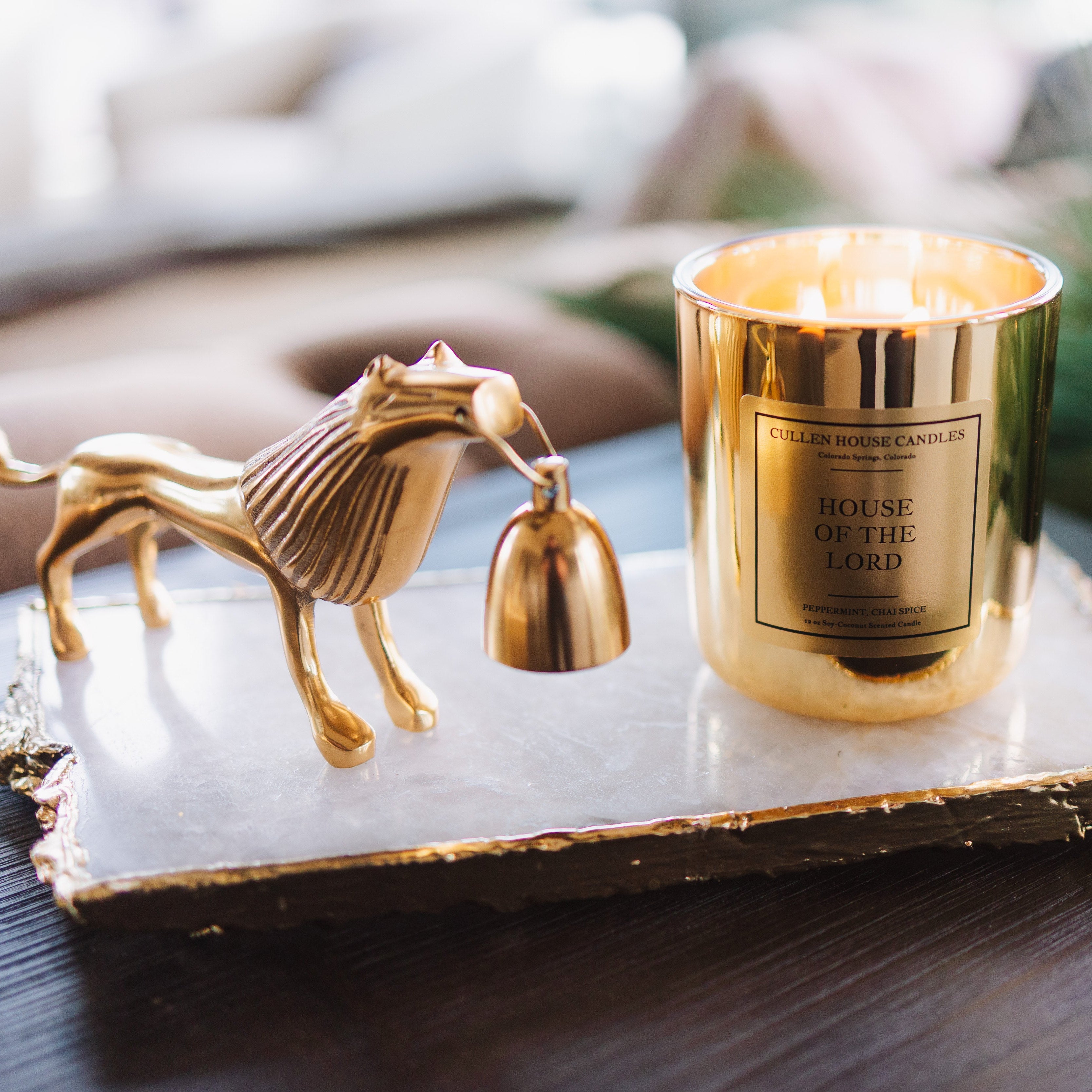 Gold candle holder with a horse design on a marble tray, featuring a lit candle.