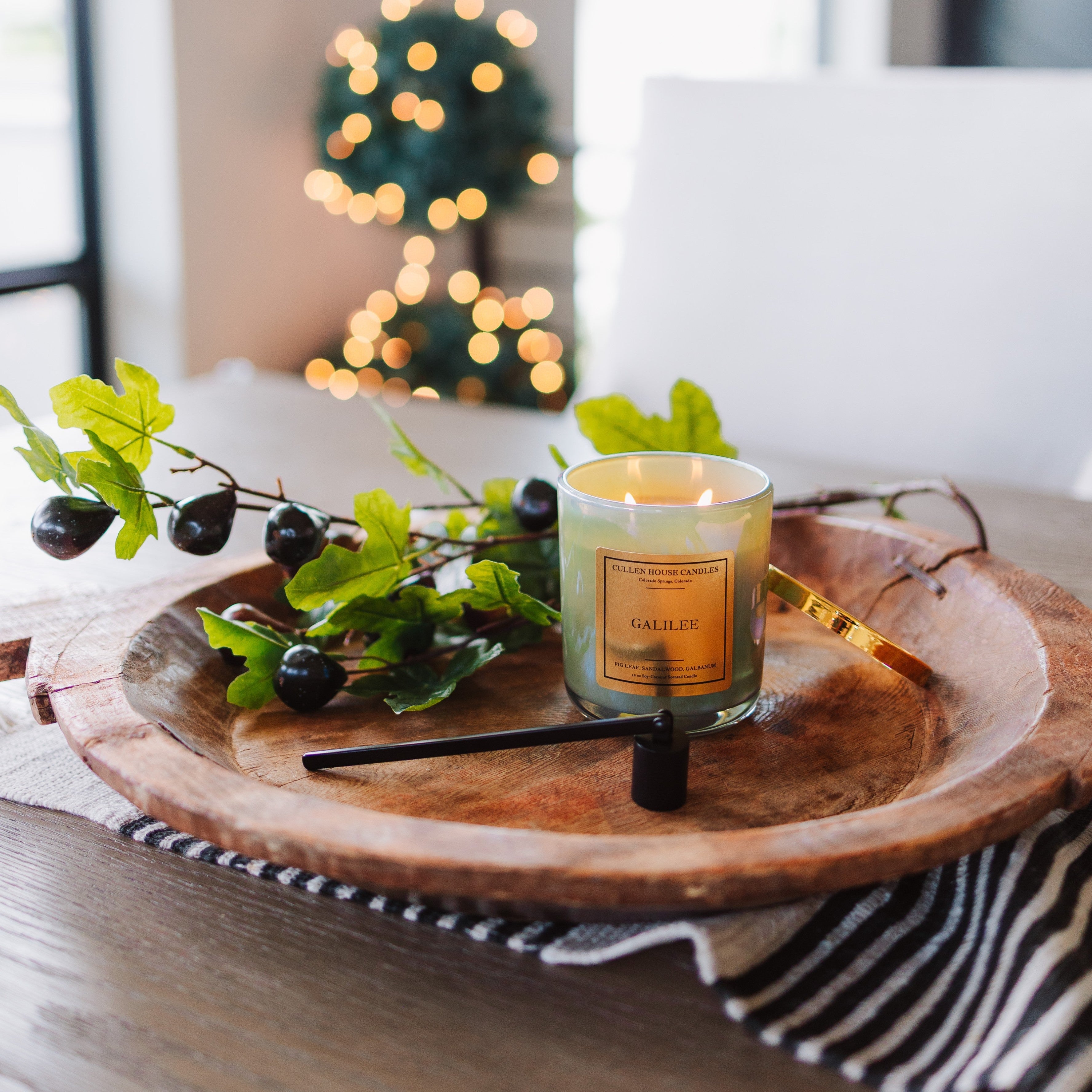 Candle on a wooden tray with decorative branches and blurred lights in the background