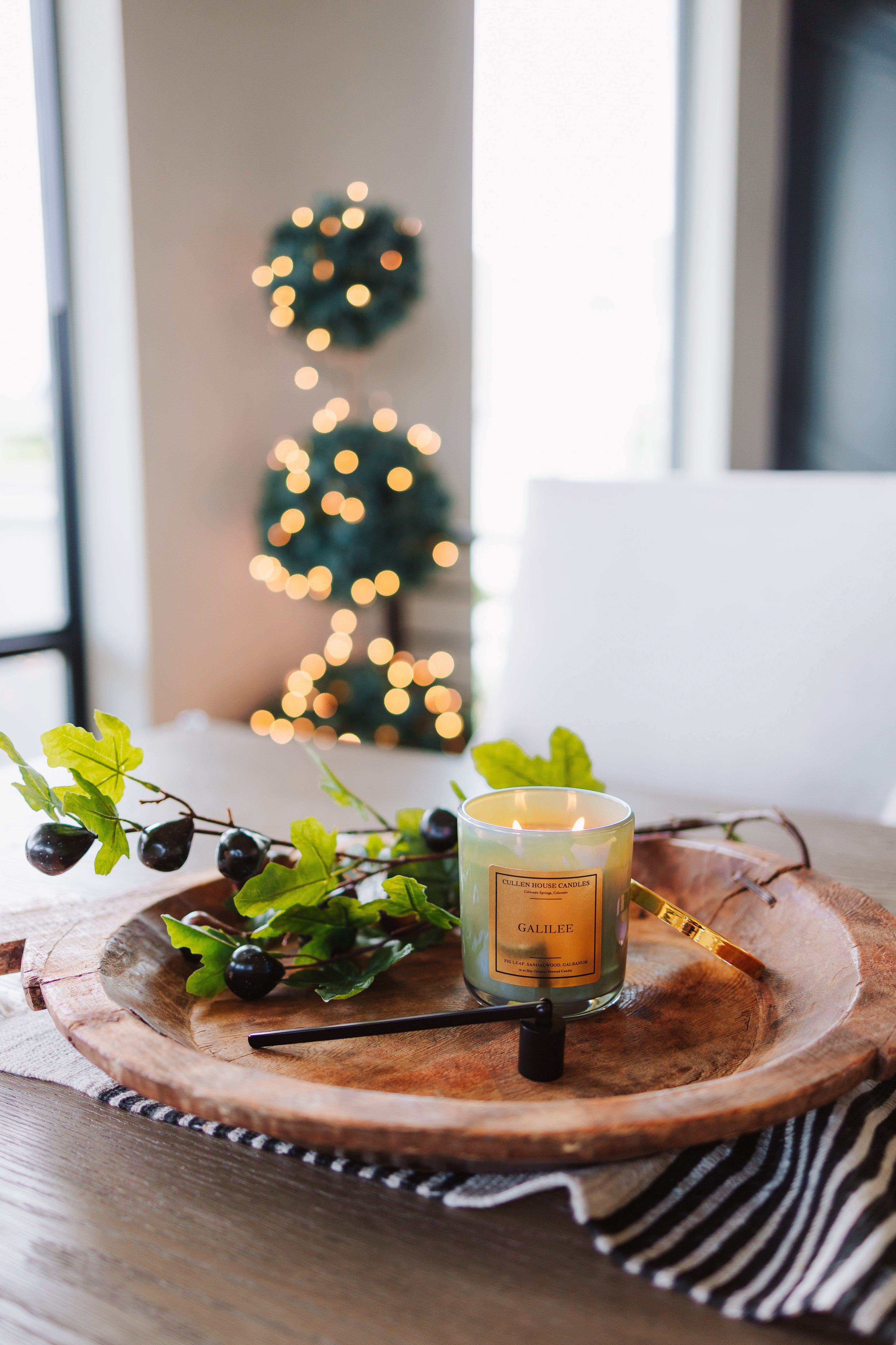 Candle on a wooden tray with decorative branches and blurred lights in the background