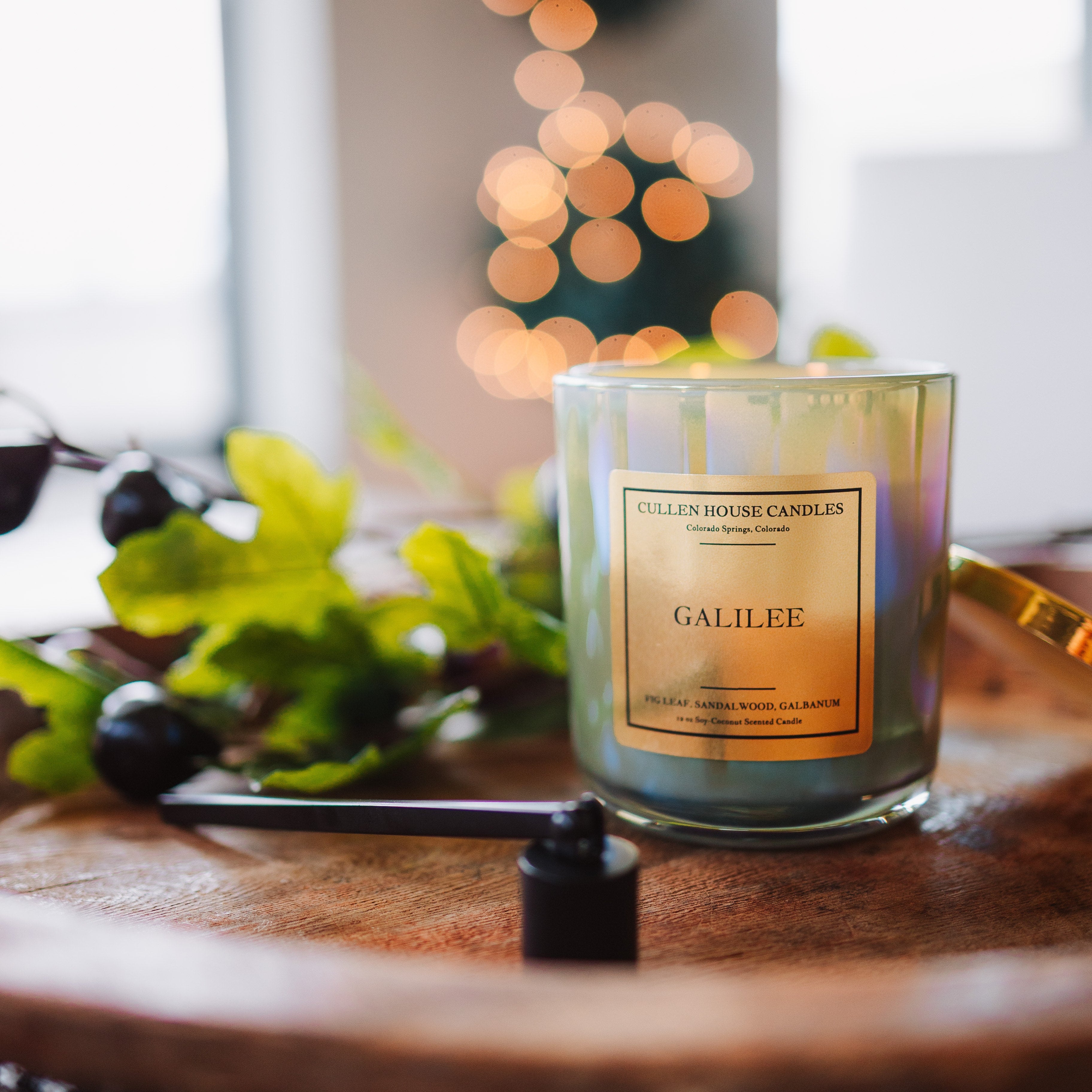 Candle labeled 'Galilee' on a wooden surface with blurred lights in the background