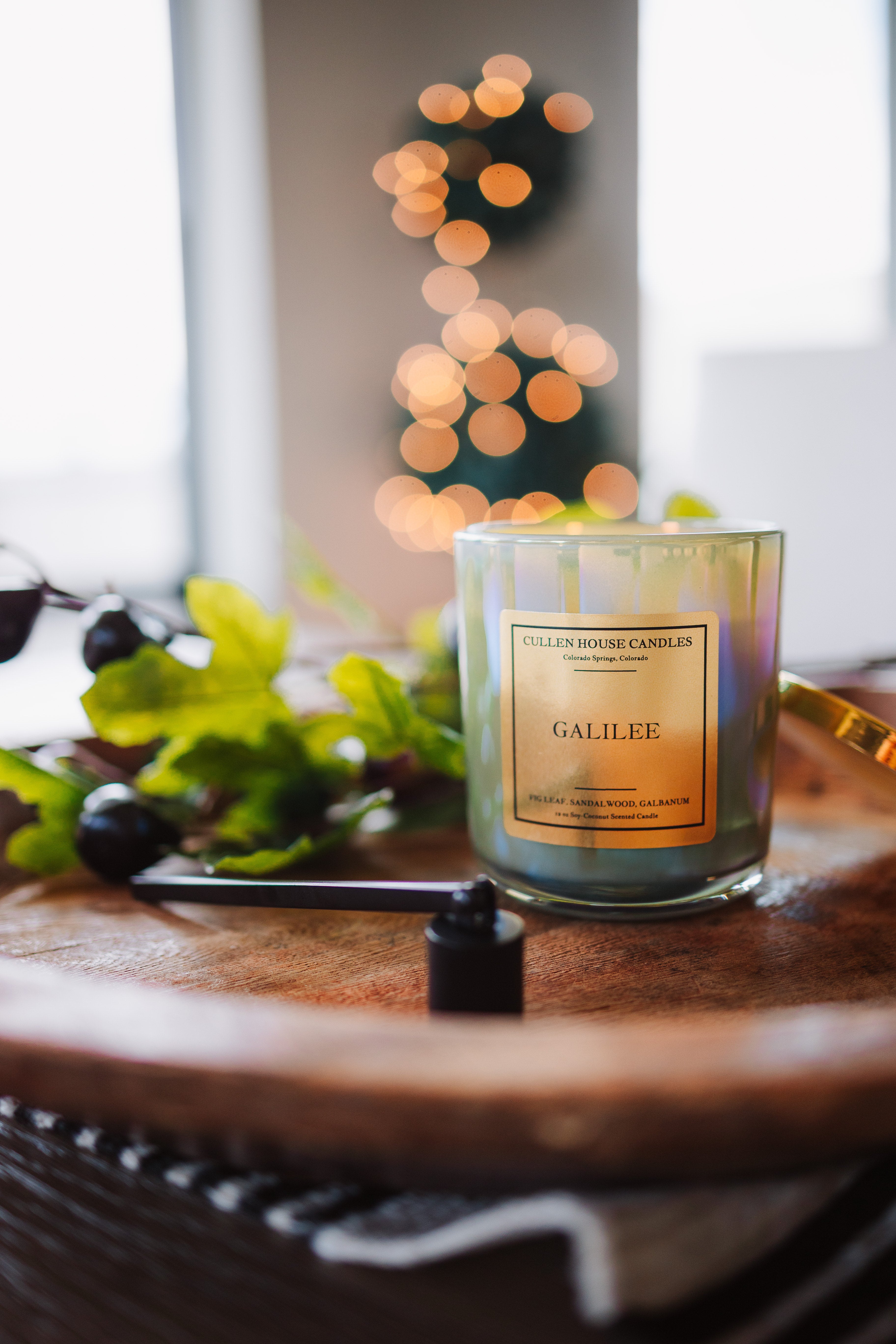Candle labeled 'Galilee' on a wooden surface with blurred lights in the background