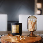 Candle with gold packaging and a glass container with matches on a wooden surface.