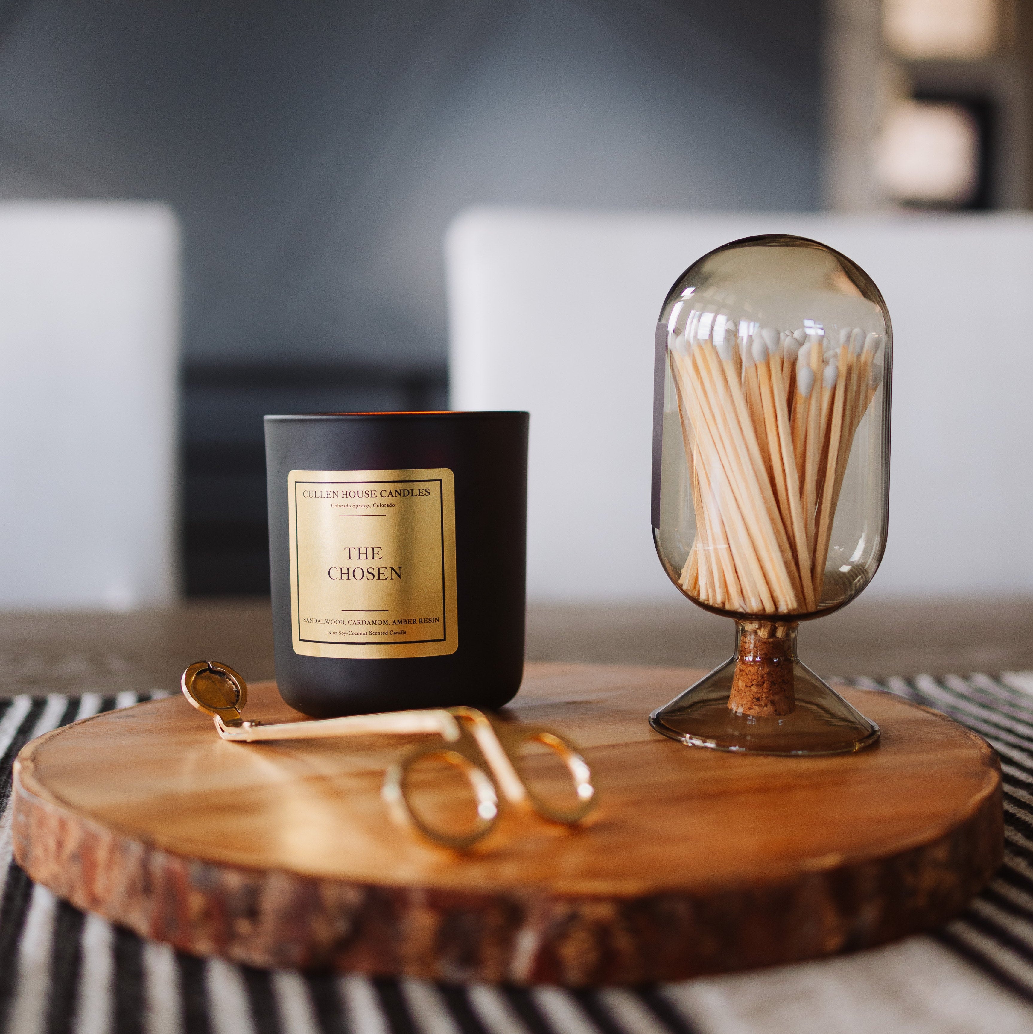 Candle with gold packaging and a glass container with matches on a wooden surface.