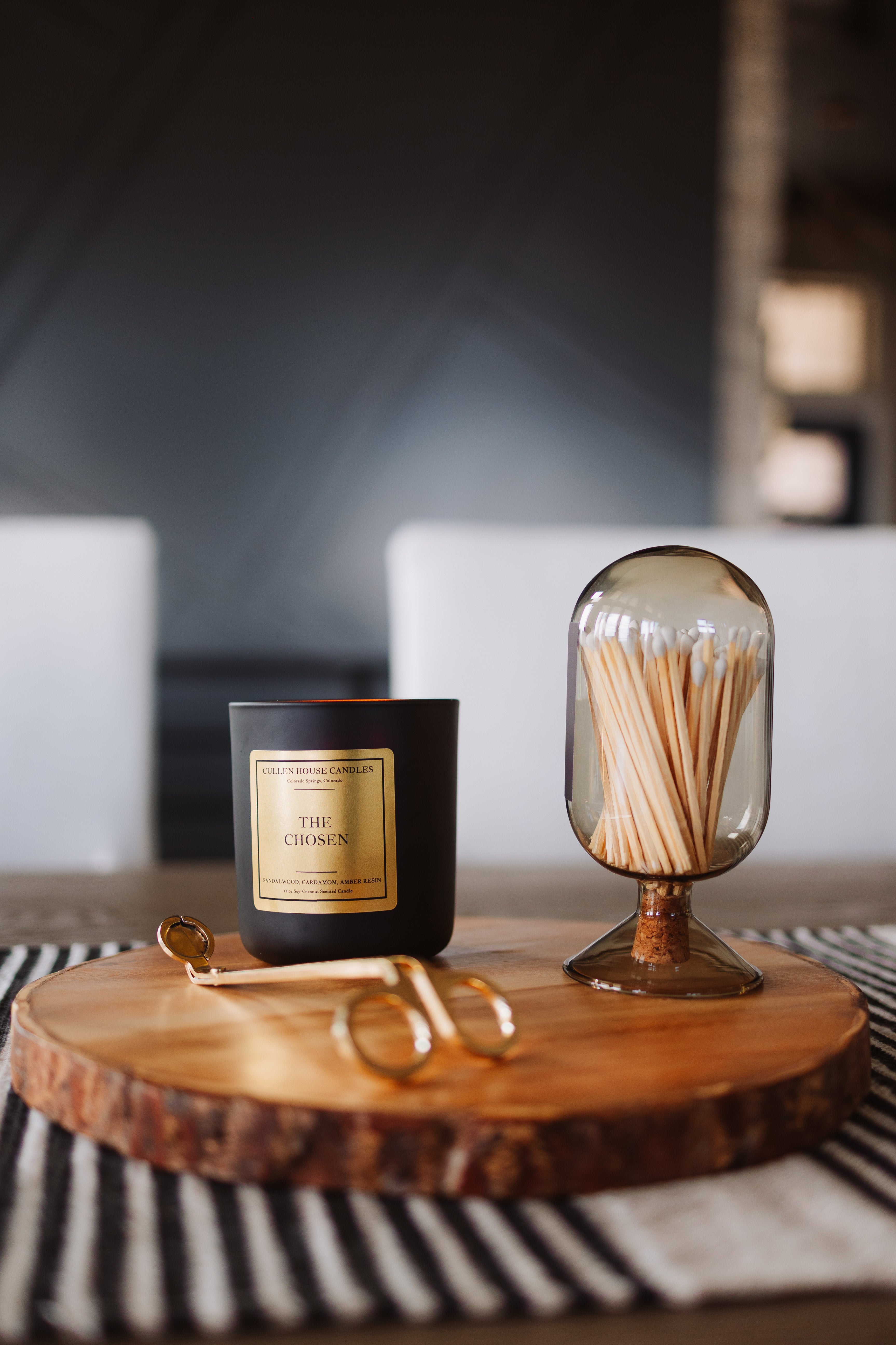Candle with gold packaging and a glass container with matches on a wooden surface.