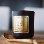 Black candle labeled 'The Chosen' on a wooden surface with a blurred background