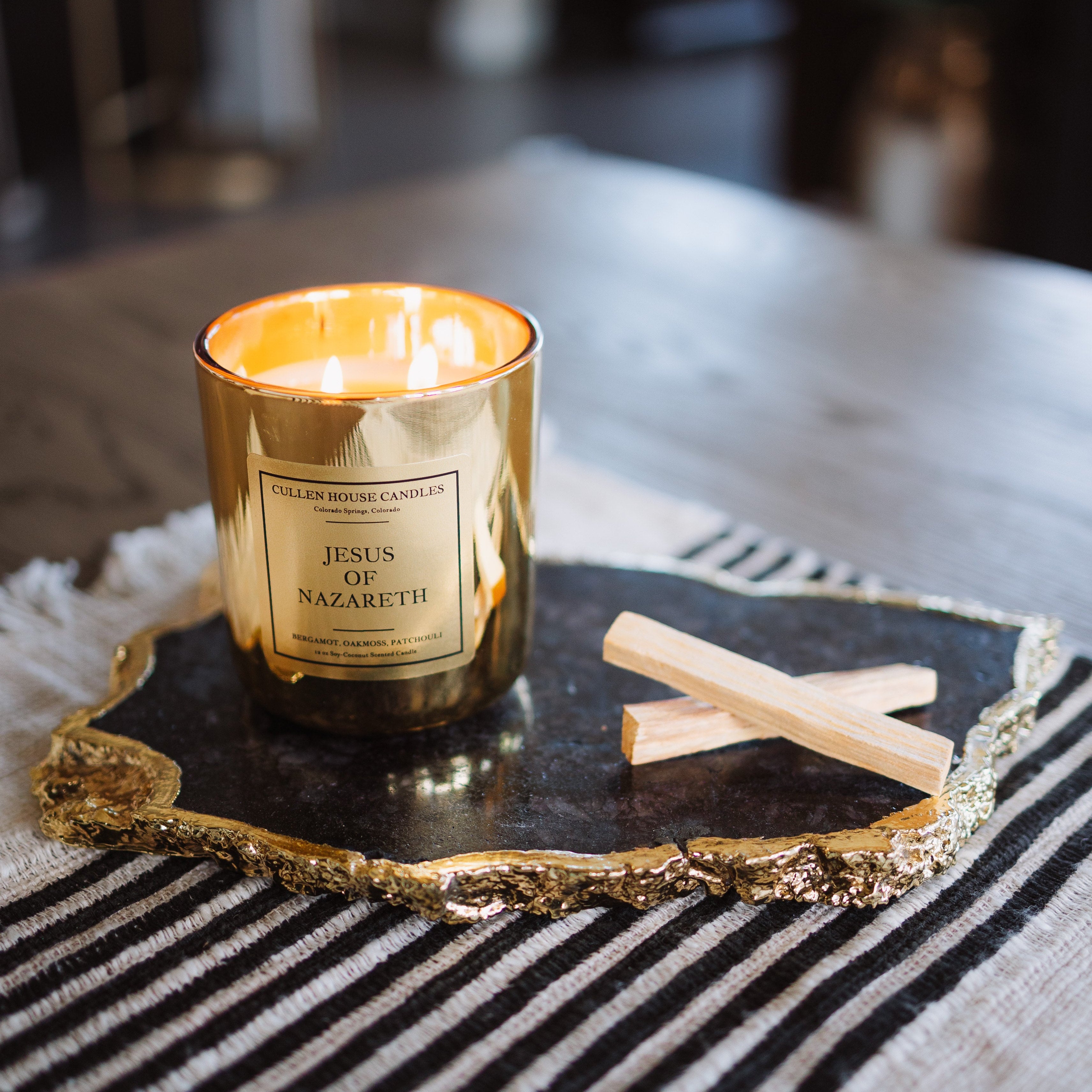 Gold candle with a label on a decorative tray on a striped surface