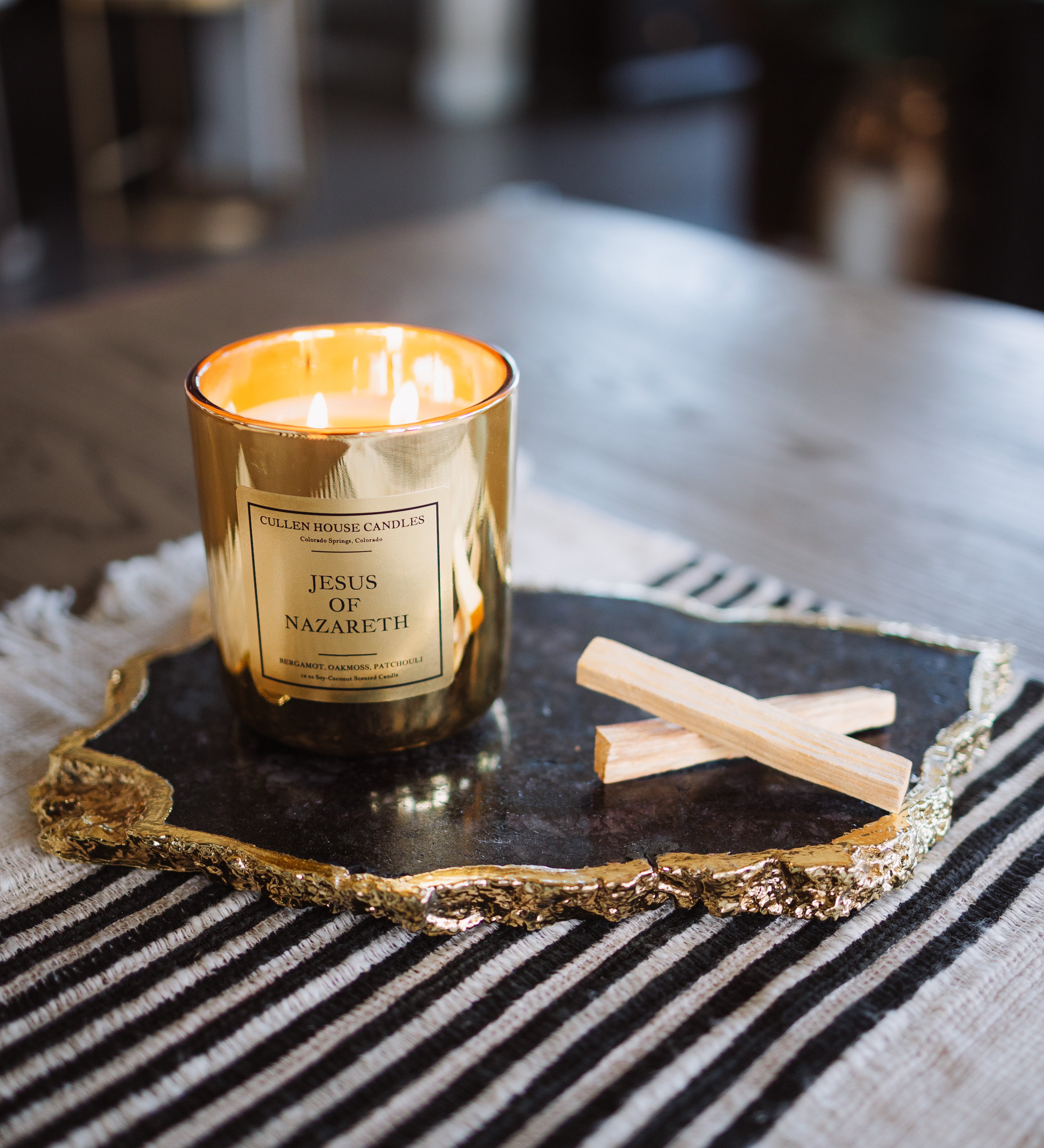 Gold candle with a label on a decorative tray on a striped surface