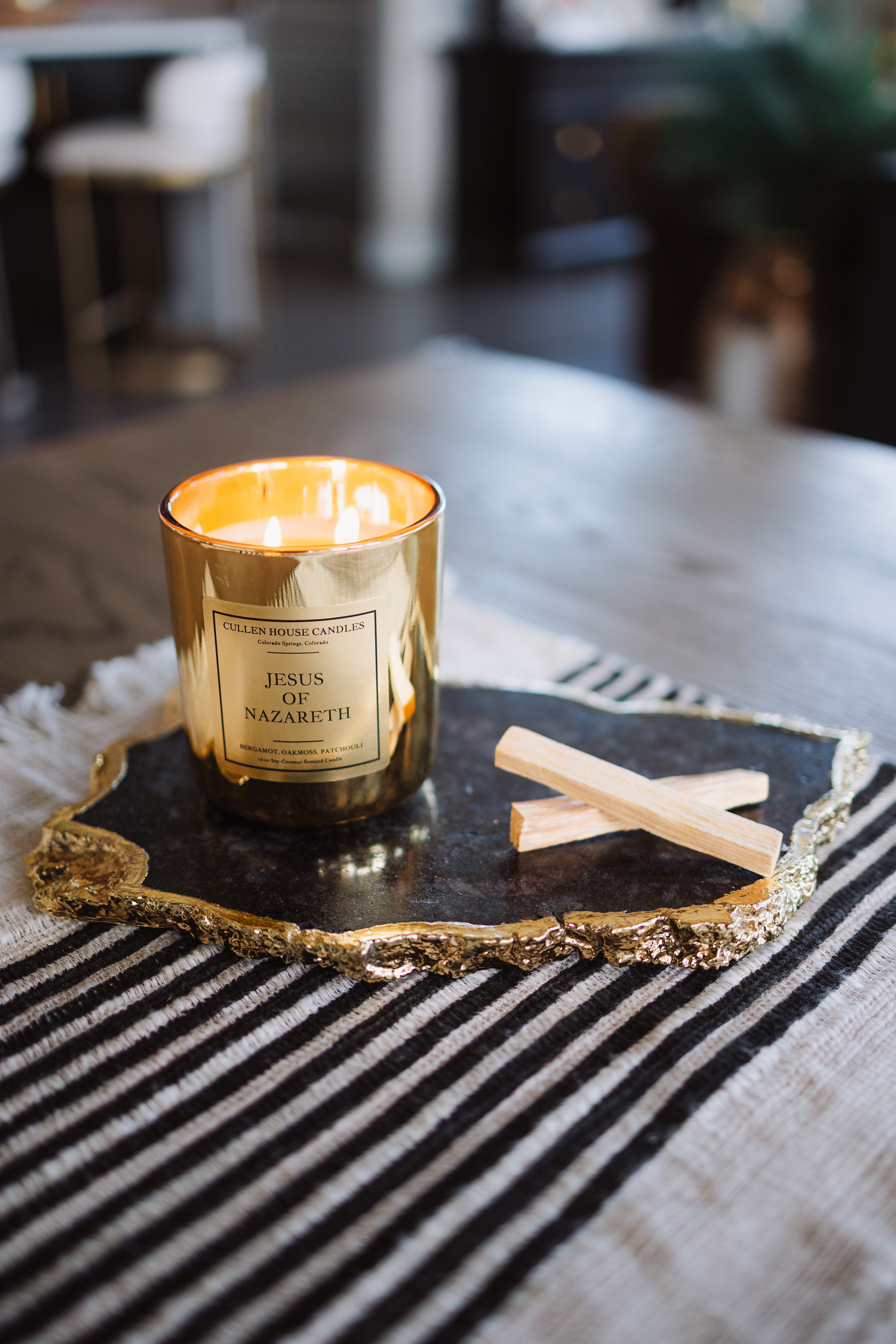 Gold candle with a label on a decorative tray on a striped surface