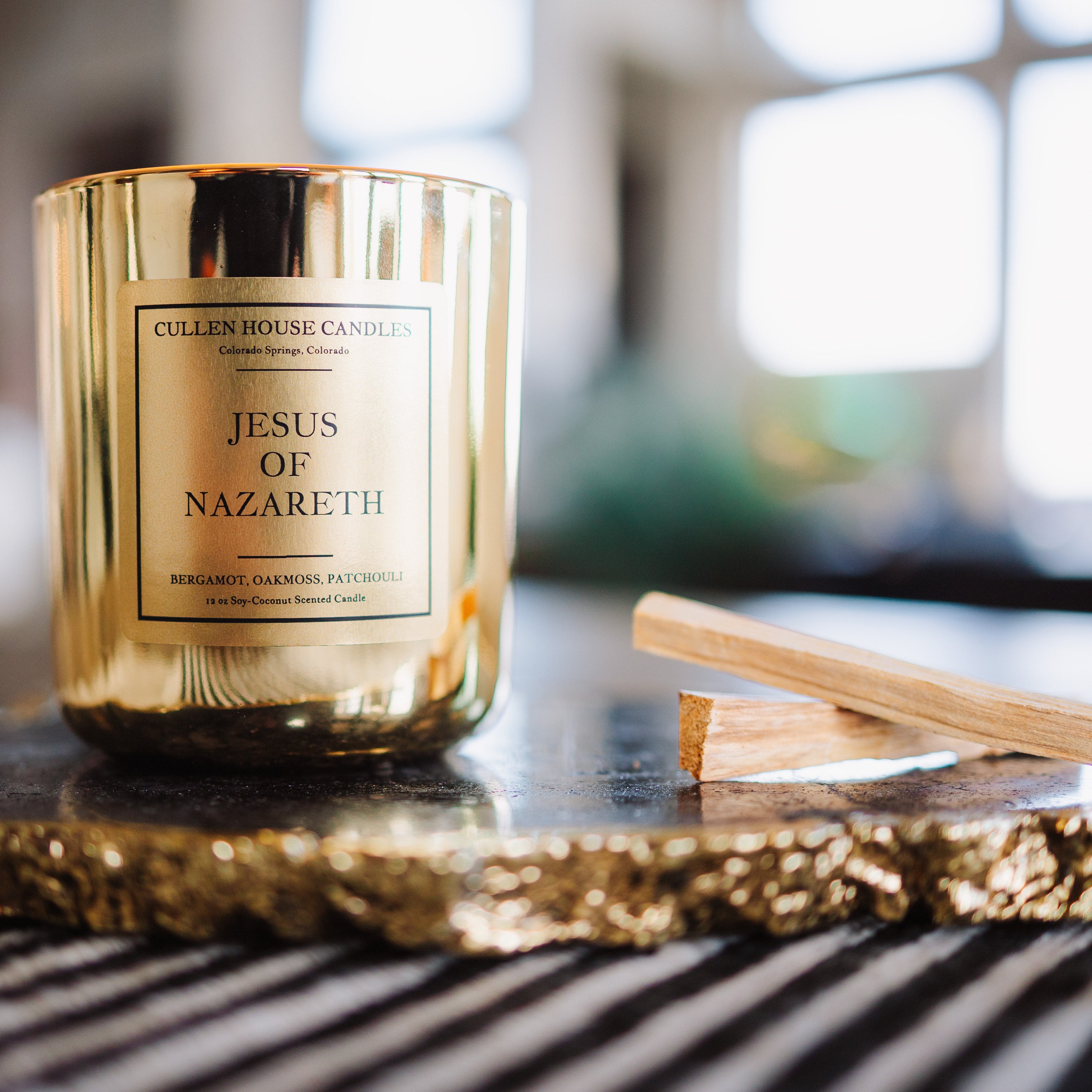 Gold candle labeled 'Jesus of Nazareth' on a decorative tray with blurred background