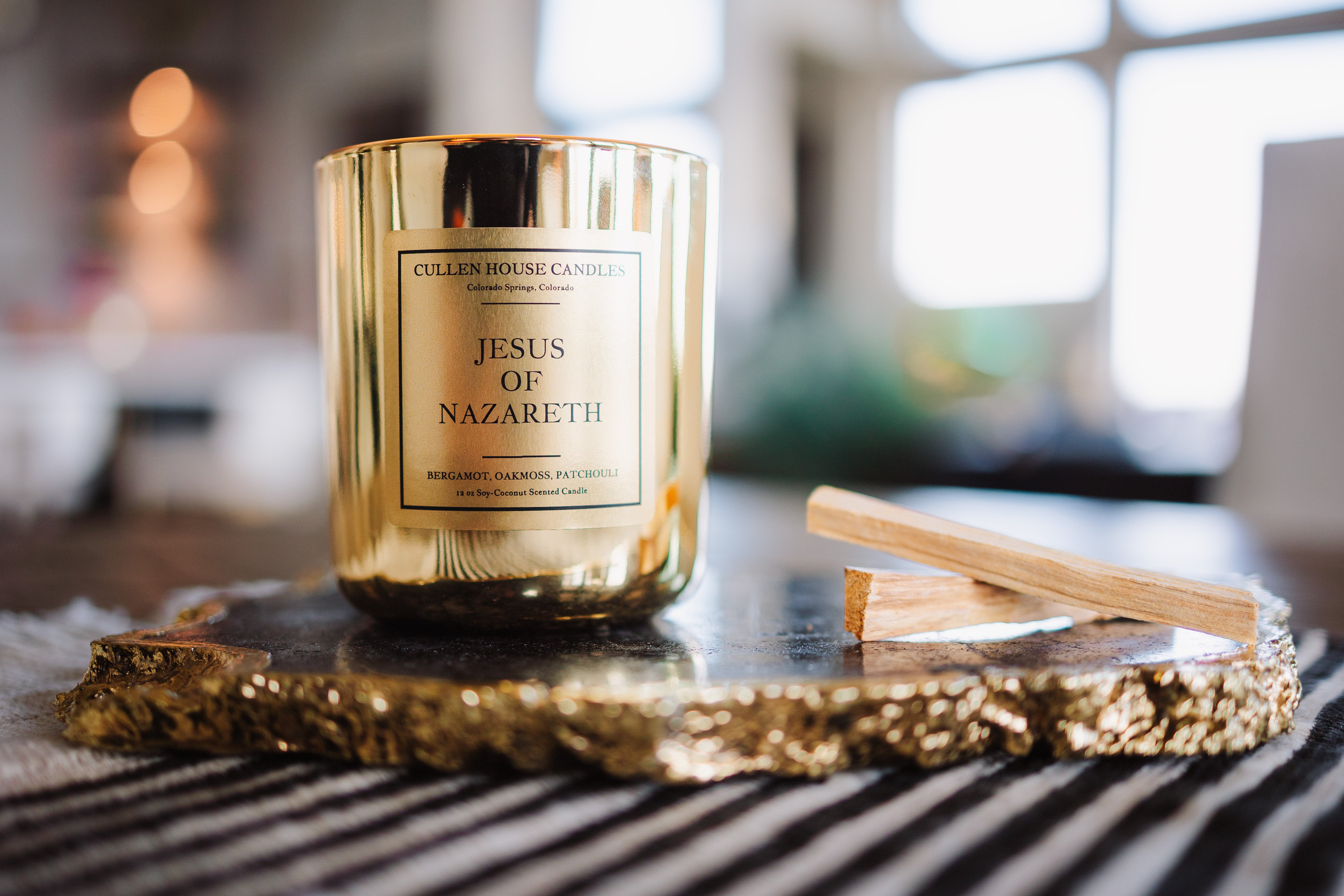 Gold candle labeled 'Jesus of Nazareth' on a decorative tray with blurred background