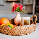 Wicker tray with fruits, a candle, and a vase with flowers on a kitchen counter.