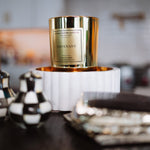 Candle with gold packaging on a decorative stand in a home setting