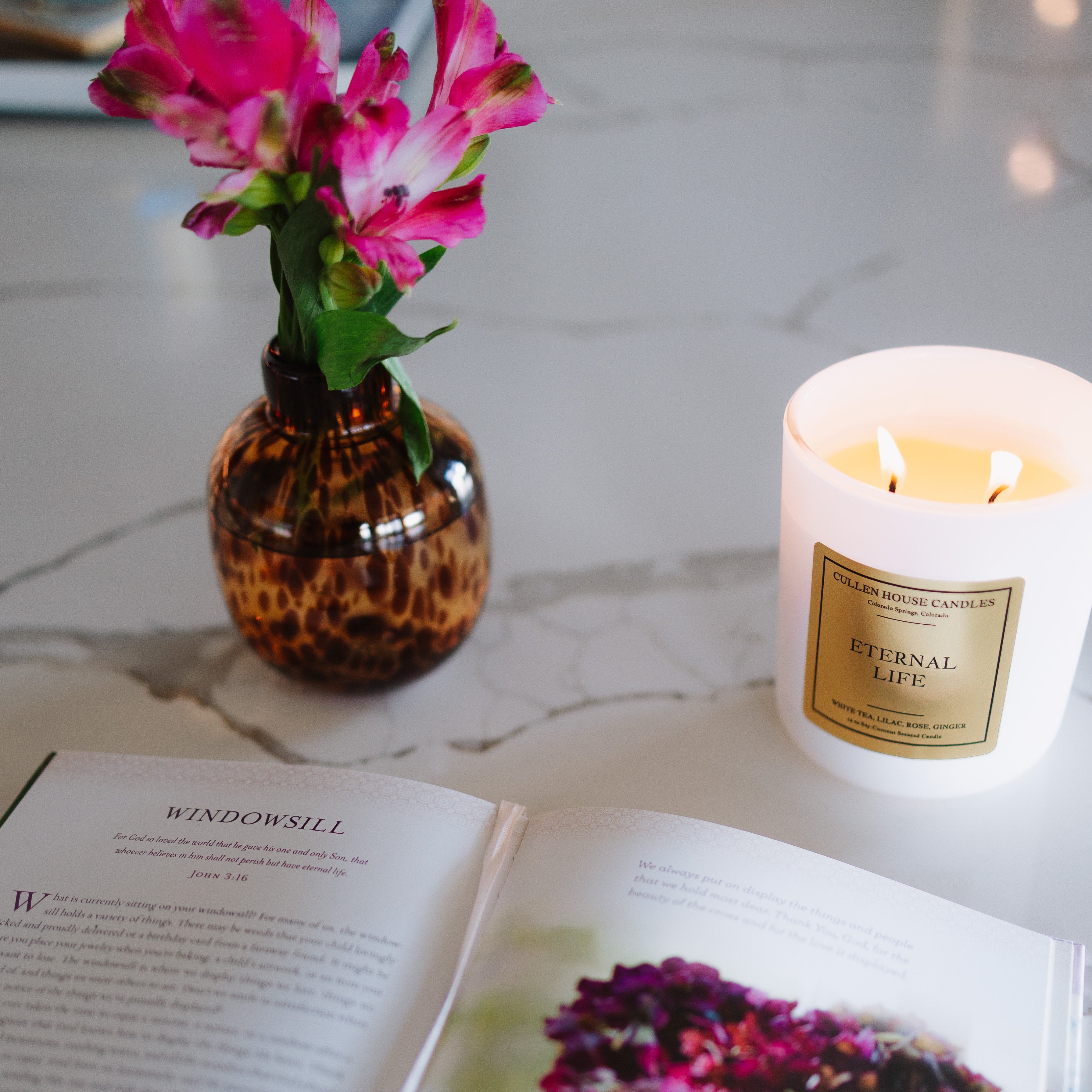 Open book with a candle and vase of flowers on a marble surface